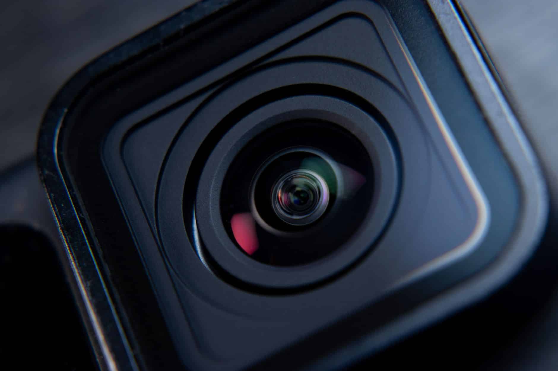 Close-up of a camera lens with reflections visible on the glass, highlighting the details of the concentric rings and the lens housing.
