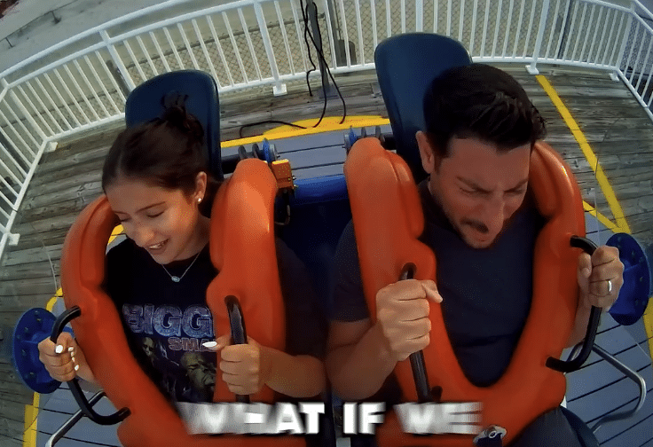 A girl and a man sit next to each other on an amusement park ride, gripping the safety bars. Both appear anxious and excited. Large white text at the bottom reads, “WHAT IF WE”.